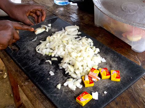African cooking, chopping onions with Maggi stock packets nearby