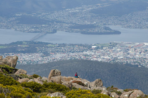 A hiker sits at the top of a mountain overlooking Hobart, Tasmania, after a hike