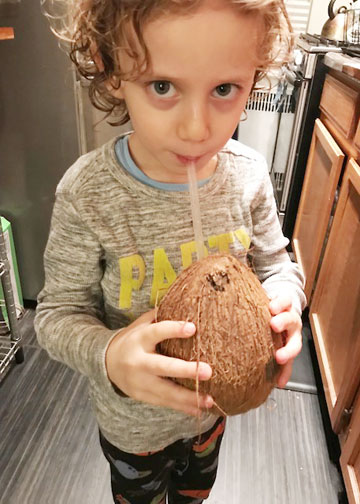 Young boy drinking coconut water from the coconut in a kitchen.