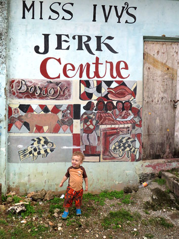 Toddler in front of jerk chicken sign in Jamaica