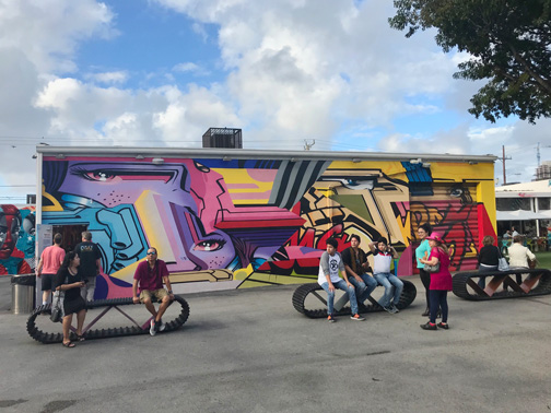 People sitting on tire-shaped benches in front of the Wynwoood Walls in Miami, Florida.