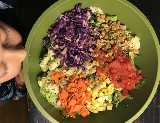 Child looking into a big bowl of colorful salad.