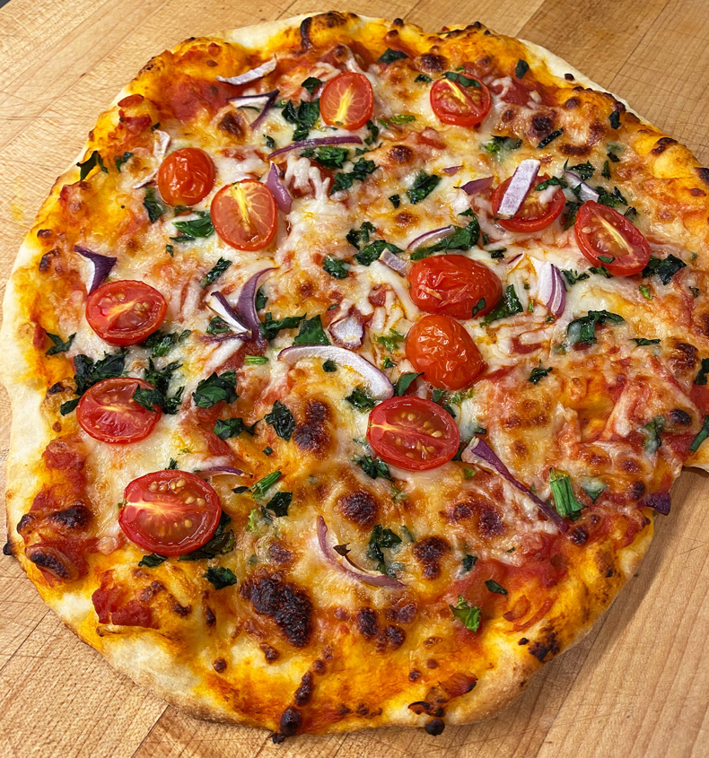 Homemade pizza topped with tomatos and onions from a pizza stone