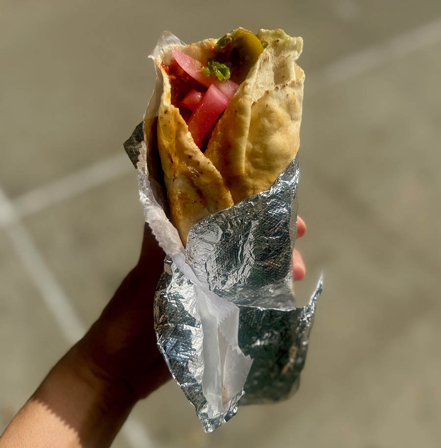 A hand holds out a chicken shawarma sandwich from Souk El Shater in Sunnyside, Queens.