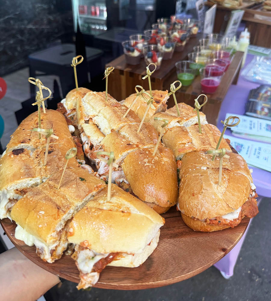 A platter of chicken parm sandwiches and display of colorful smoothies at Empire Shop in Sunnyside, Queens, for Taste of Sunnyside 2024