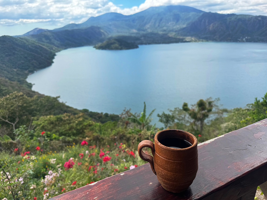 A cup of coffee in front of Lago de Coatepeque, a volcanic caldera lake ringed by volcanoes and flowers, in El Salvador.