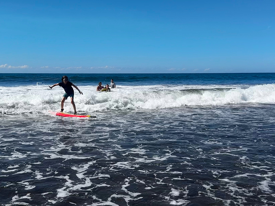 A child stands up on a surfboard during a surf lesson in El Salvador.
